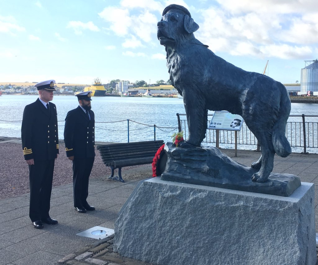 Two military men standing in front of the statue of Bamse